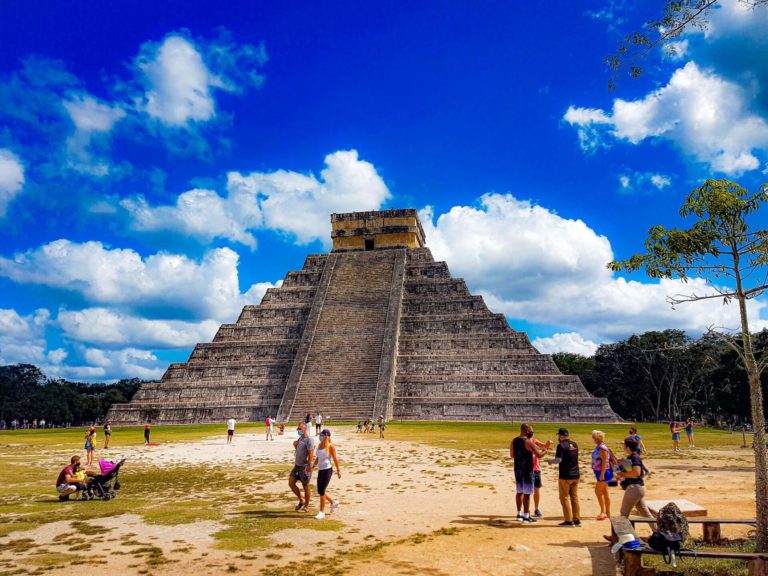 a group of people on a beach with Chichen Itza in the background